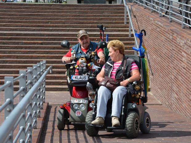 deux personnes se déplace en extérieur en fauteuil roulant électrique